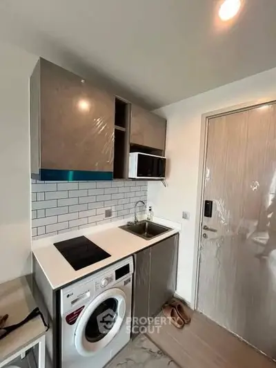 Modern compact kitchen with washing machine and microwave in sleek apartment.