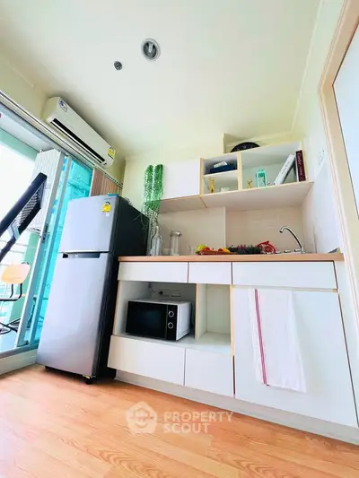 Modern kitchen with sleek cabinetry, microwave, and fridge in a bright apartment setting.