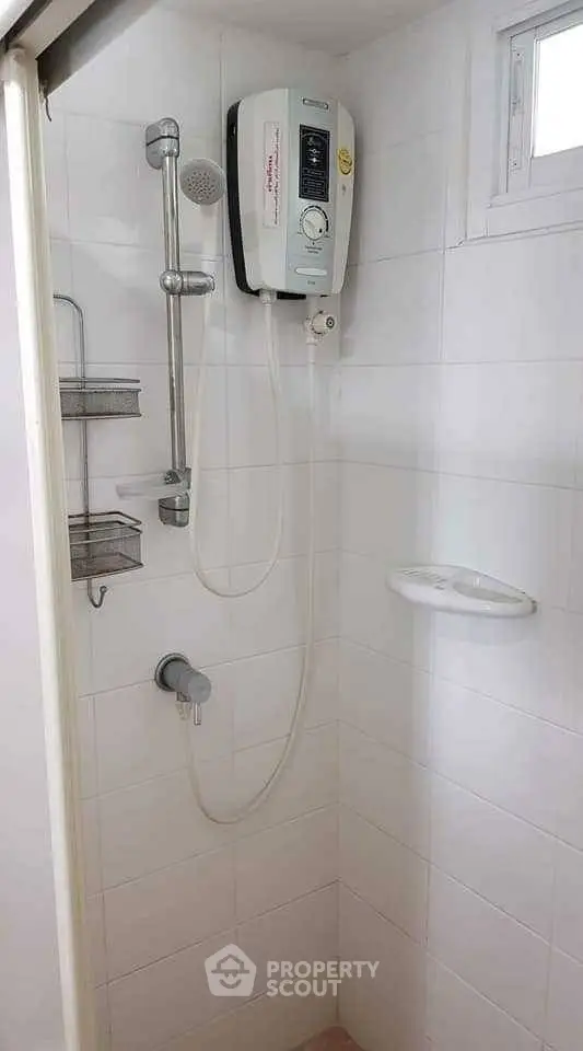 Compact bathroom shower area with electric water heater and white tiles.