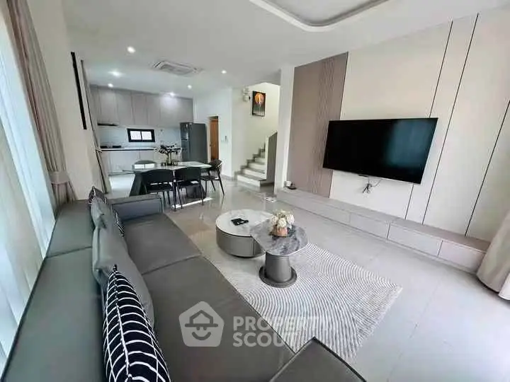 Modern living room with sleek design and open kitchen layout, featuring a large TV and stylish furniture.