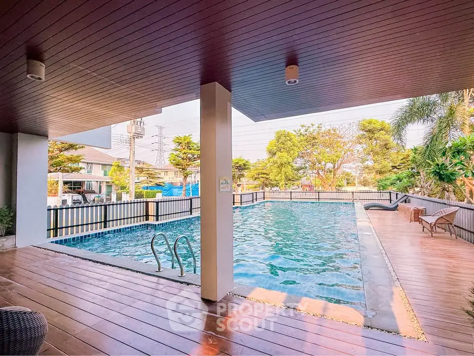 Luxurious residential pool area with wooden deck and lush greenery, perfect for relaxation and leisure.