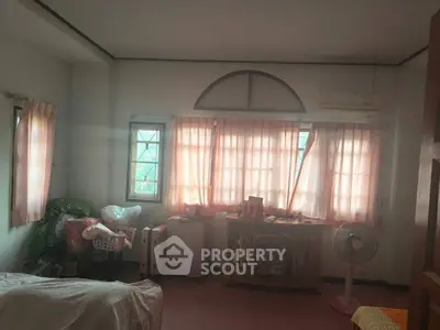 Cozy bedroom with soft lighting and simple decor, featuring a fan and ample natural light.