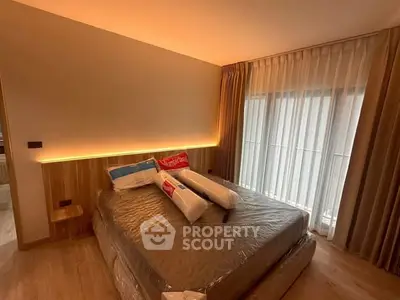 Modern bedroom with cozy lighting and large window draped with sheer curtains.