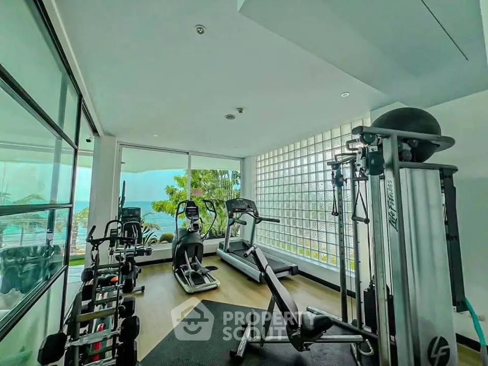 Modern gym with ocean view, featuring state-of-the-art equipment and floor-to-ceiling windows.