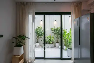 Modern kitchen with large glass doors opening to a lush patio garden, featuring sleek appliances and elegant decor.
