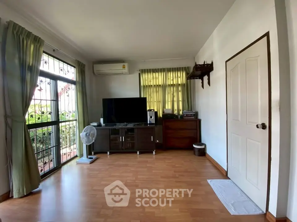 Spacious living room with wooden flooring and large window, featuring modern entertainment setup.