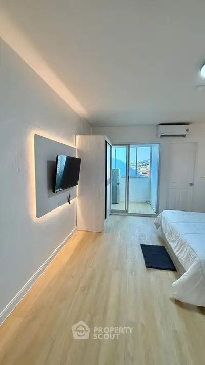 Modern bedroom with wall-mounted TV and balcony access, featuring sleek design and natural light.