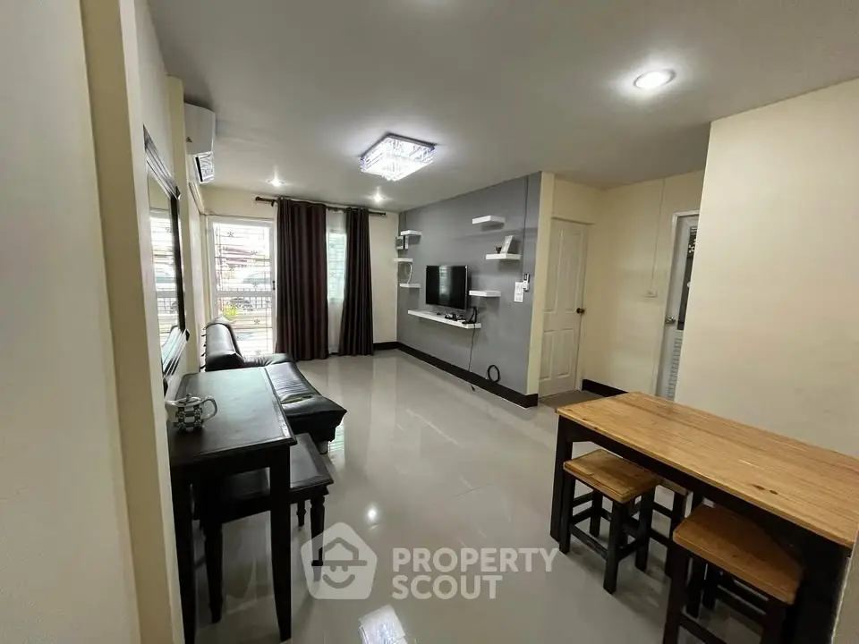 Modern living room with sleek design and natural light, featuring a cozy dining area and wall-mounted TV.