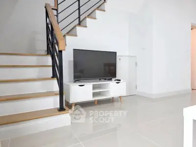 Modern living room with sleek staircase and TV unit, showcasing minimalist design and glossy tiled flooring.