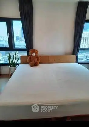 Cozy bedroom with large windows and city view, featuring a plush teddy bear on the bed.