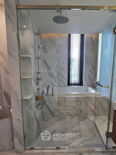 Luxurious marble bathroom with glass shower and bathtub, featuring modern fixtures and natural light.