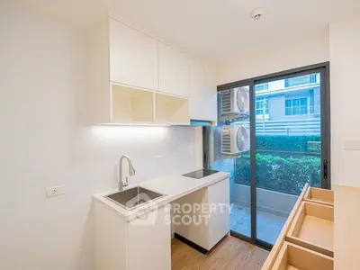 Modern kitchen with sleek design and garden view, featuring built-in cabinets and stainless steel sink.