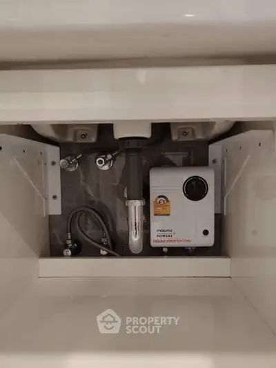 Under-sink plumbing with water heater in modern kitchen cabinet.