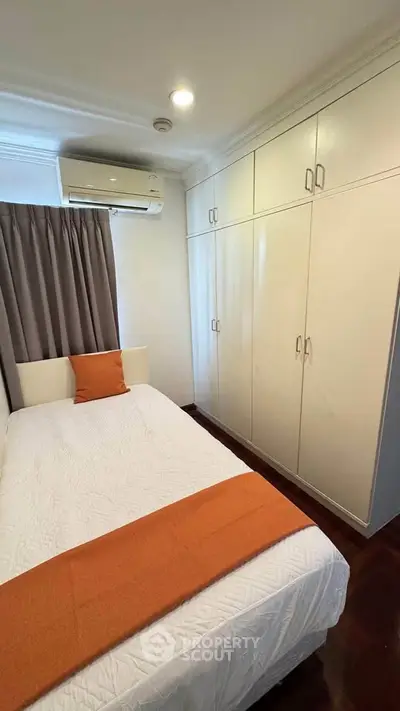Cozy bedroom with built-in wardrobe and air conditioning, featuring warm orange accents.