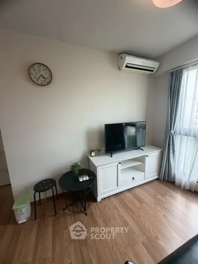 Cozy living room with wooden flooring, TV setup, and natural light from large window.