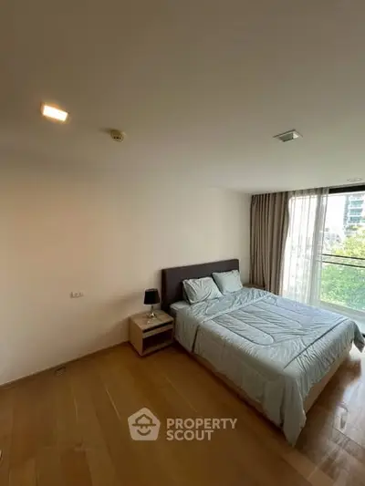 Spacious bedroom with large window and modern furnishings in a high-rise apartment.