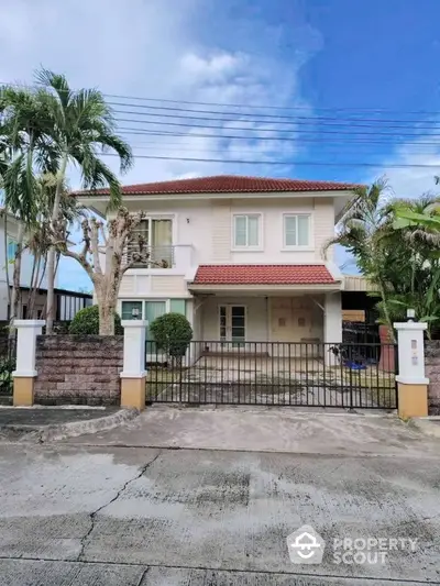 Charming two-story house with red roof and lush palm trees in a serene neighborhood.