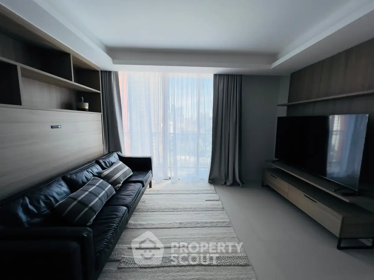 Modern living room with sleek furniture and large TV, featuring floor-to-ceiling windows for natural light.