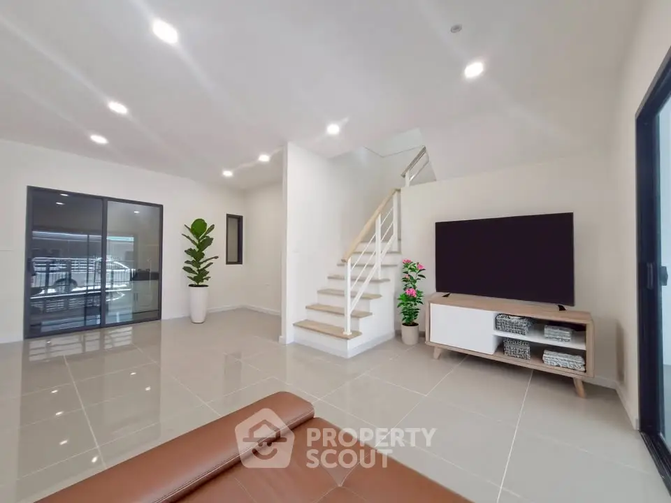 Spacious modern living room with sleek staircase and large TV, perfect for family gatherings.