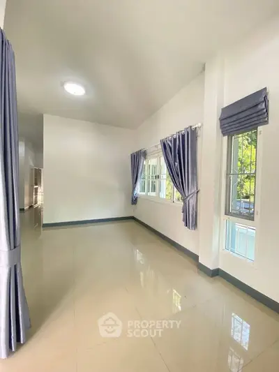 Spacious and bright living room with large windows and elegant curtains, perfect for natural light lovers.