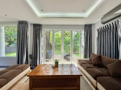 Spacious living room with large windows and garden view, featuring elegant sofas and a wooden coffee table.