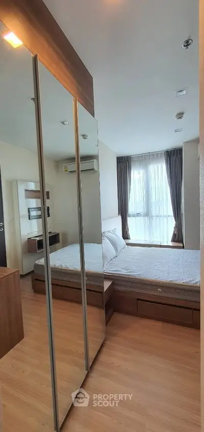 Modern bedroom with mirrored wardrobe and large window offering natural light.