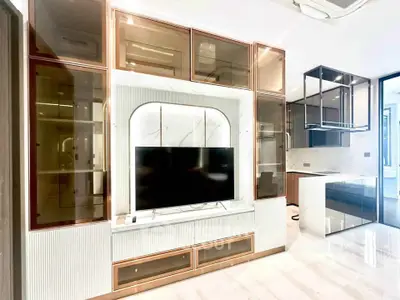 Modern living room with sleek cabinetry and large TV, featuring open kitchen layout and stylish design.