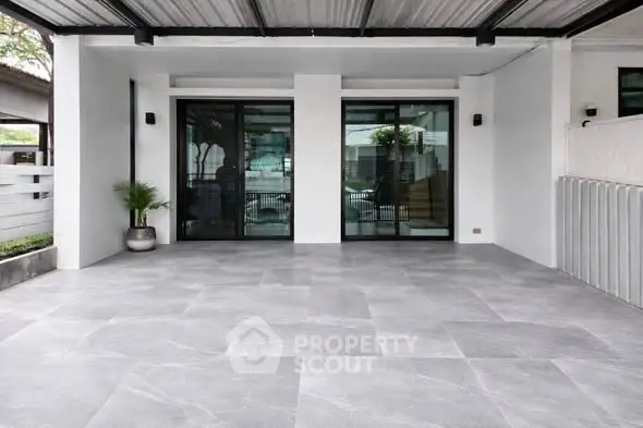 Modern home exterior with spacious tiled patio and large glass doors.