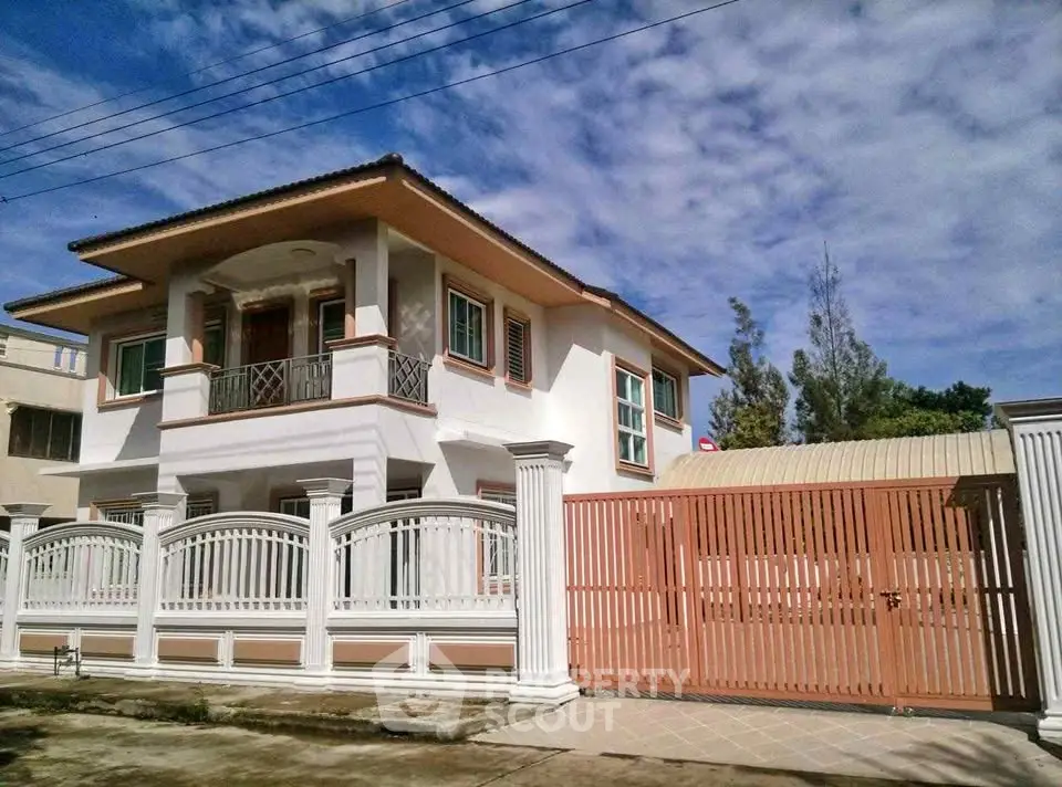 Elegant two-story house with gated entrance and spacious balcony under a clear blue sky.