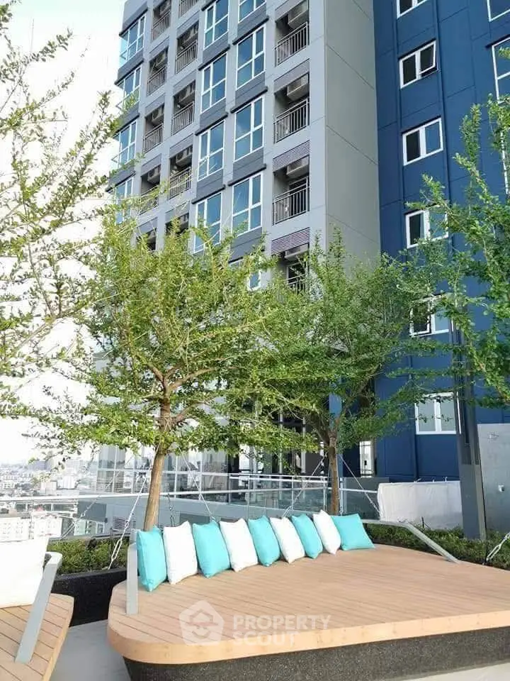 Modern high-rise building with rooftop garden and seating area, offering stunning city views.