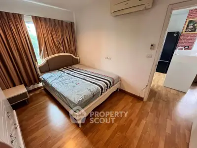 Cozy bedroom with wooden flooring and air conditioning, featuring a stylish bed and elegant curtains.