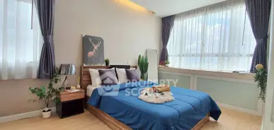 Spacious bedroom with large windows and modern decor, featuring a cozy blue bedspread.