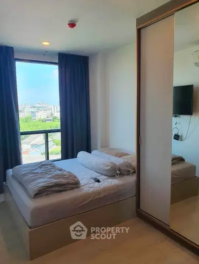 Bright and airy bedroom with a plush bed, floor-to-ceiling windows offering a city view, and a large mirror wardrobe, perfect for urban living.