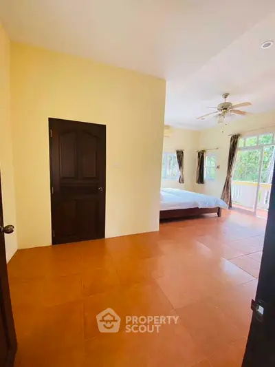 Spacious bedroom with large windows and balcony access, featuring warm tile flooring and ceiling fan.