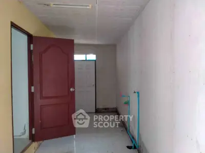 Spacious interior with potential for renovation, featuring a red door and plumbing fixtures.