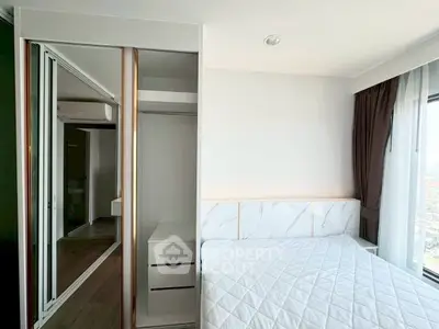 Modern bedroom with mirrored closet and large window offering city views.