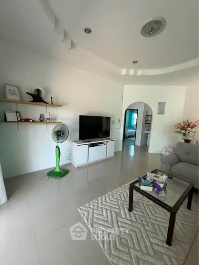 Spacious living room with modern decor and sleek tile flooring, featuring a cozy seating area and entertainment setup.