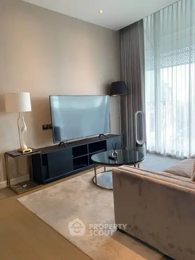 Modern living room with sleek furniture and large TV, featuring floor-to-ceiling windows for natural light.