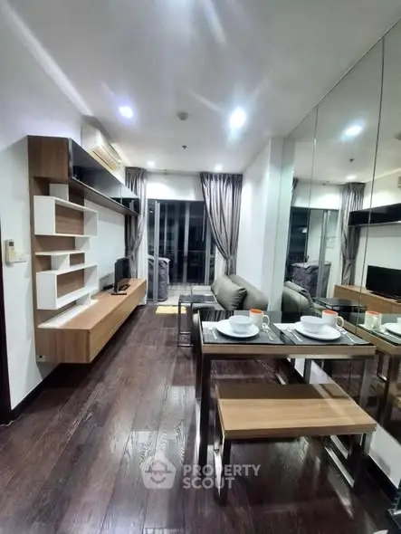 Modern living room with sleek furniture and dining area, featuring dark wood flooring and large mirror.