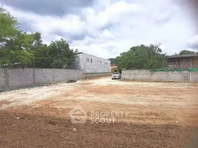 Spacious vacant land plot ideal for development with surrounding walls and trees.