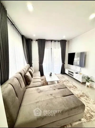 Modern living room with plush sofa, large windows, and wall-mounted TV for a cozy ambiance.