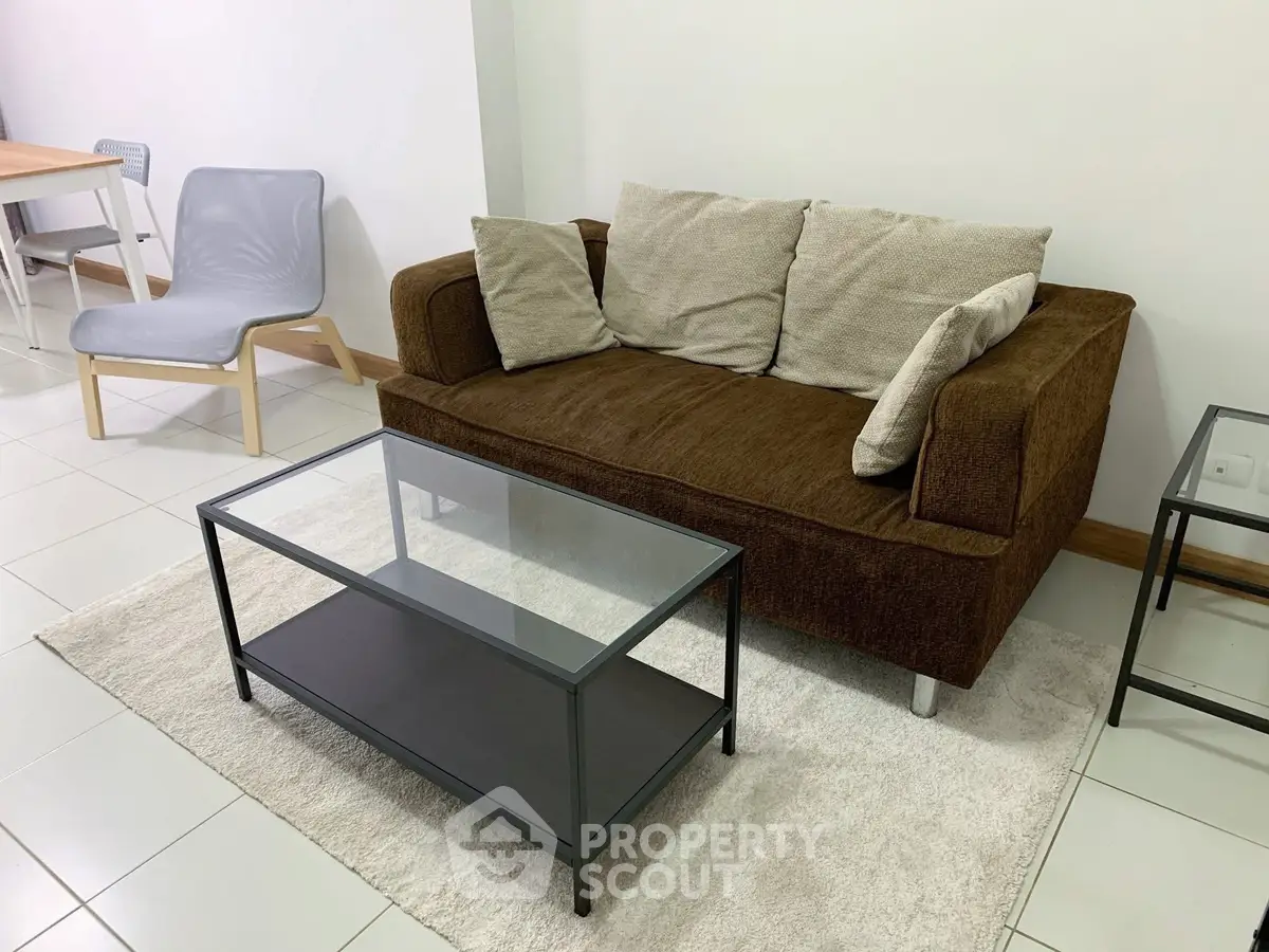 Cozy living room with modern brown sofa and glass coffee table on white tiled floor.