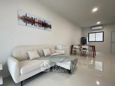 Modern living room with sleek white sofa and dining area in open layout apartment.