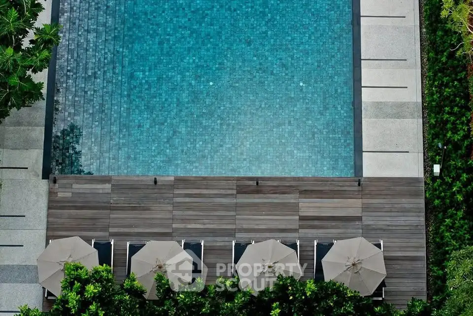 Luxurious outdoor pool area with elegant wooden deck and lush greenery, perfect for relaxation and leisure.