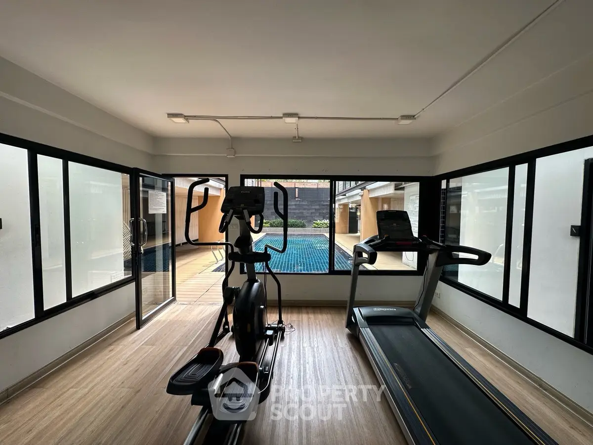 Modern gym with treadmill and elliptical overlooking a pool area