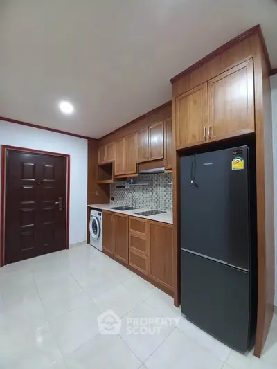 Modern kitchen with wooden cabinets, fridge, and washing machine in a cozy apartment.