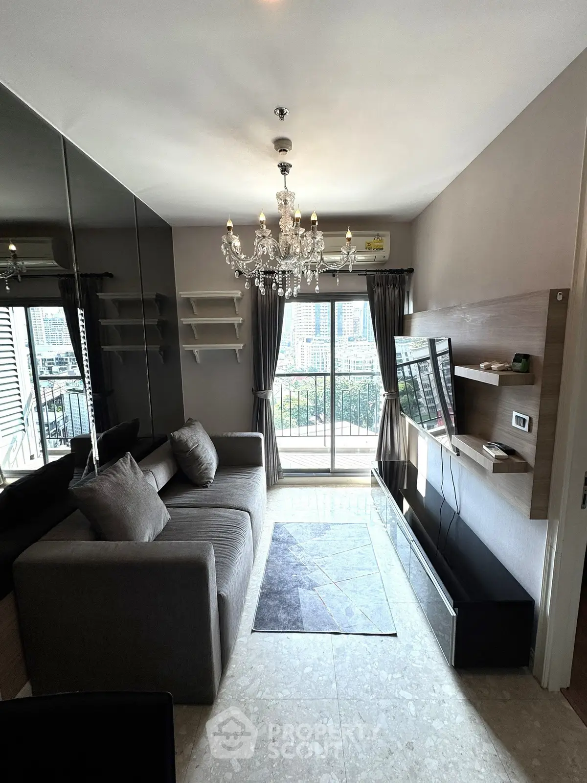 Modern living room with chandelier, sofa, and city view balcony in a stylish apartment.