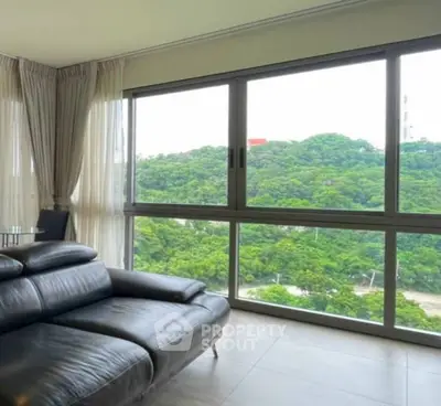 Spacious living room with large windows offering stunning green views, featuring modern leather sofa.