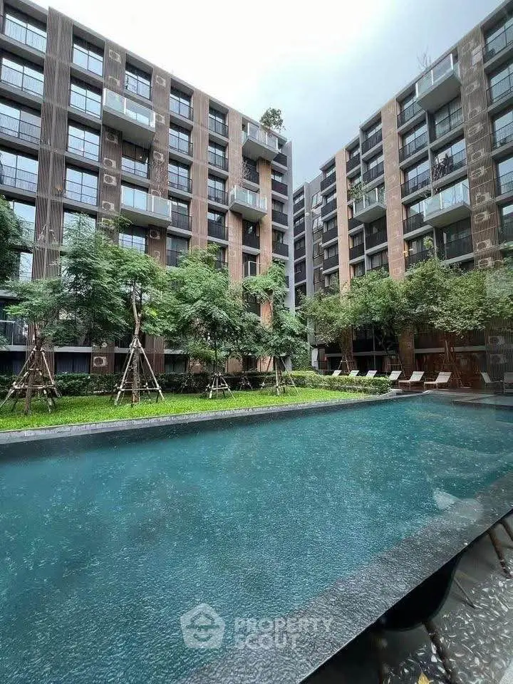 Modern apartment complex with pool and lush greenery, offering serene urban living.