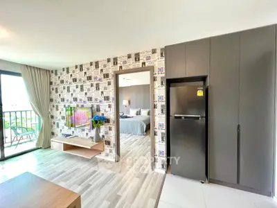 Modern living room with stylish decor and view into a cozy bedroom, featuring a sleek fridge and balcony access.
